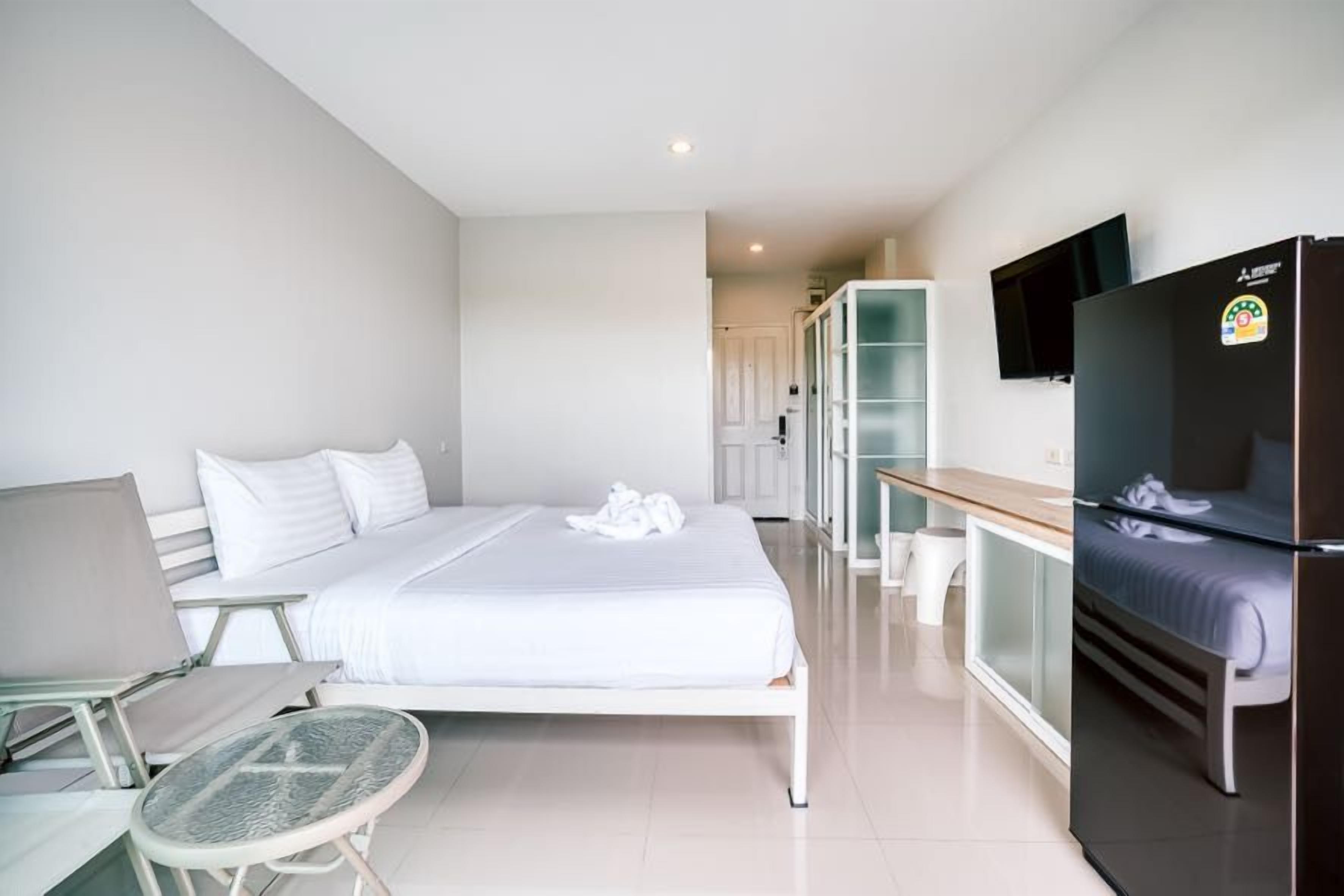 A hotel room with a bed, a desk, a chair, a television, and a refrigerator.