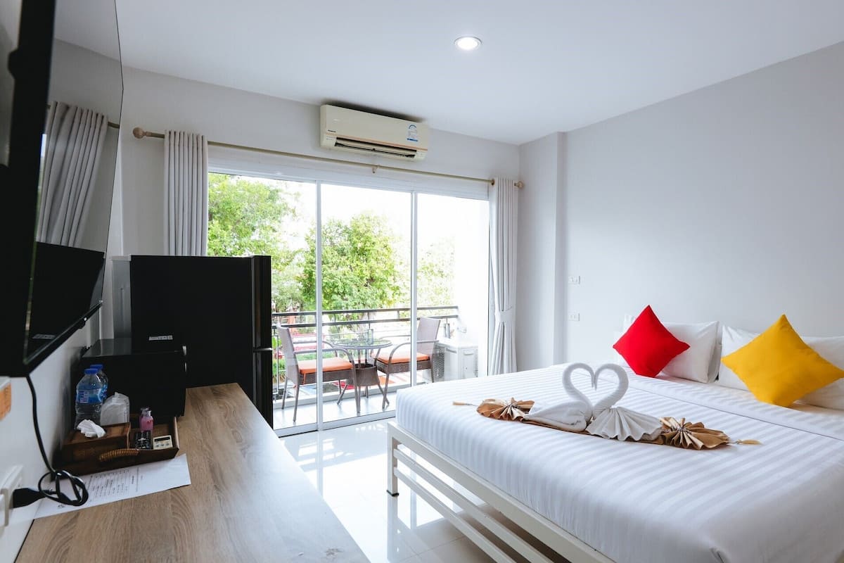 Una habitación de hotel con cama, escritorio, televisor y balcón con vistas a árboles.
