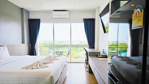 Ein Hotelzimmer mit zwei Betten, einem Balkon mit Tisch und Stühlen sowie einem großen Fernseher.