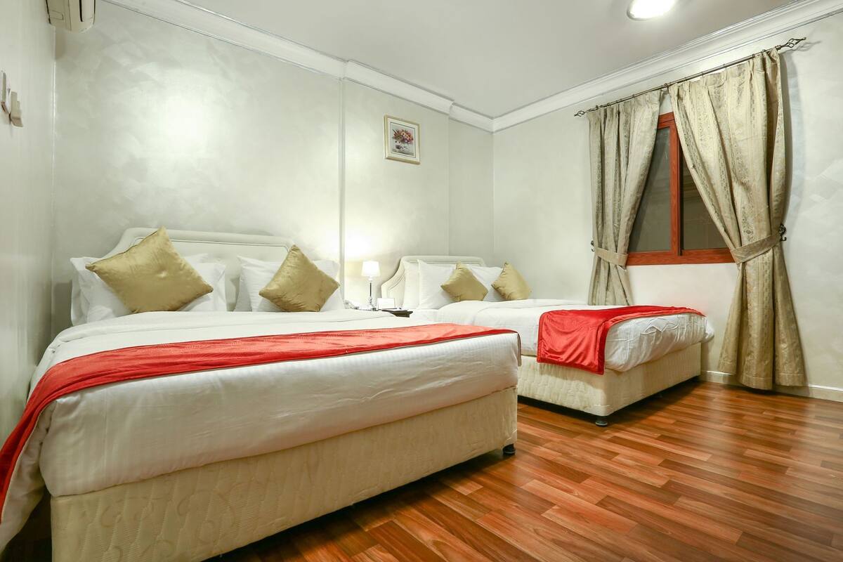 A hotel room with two beds, a wooden floor, a window with curtains, and a wall-mounted picture.