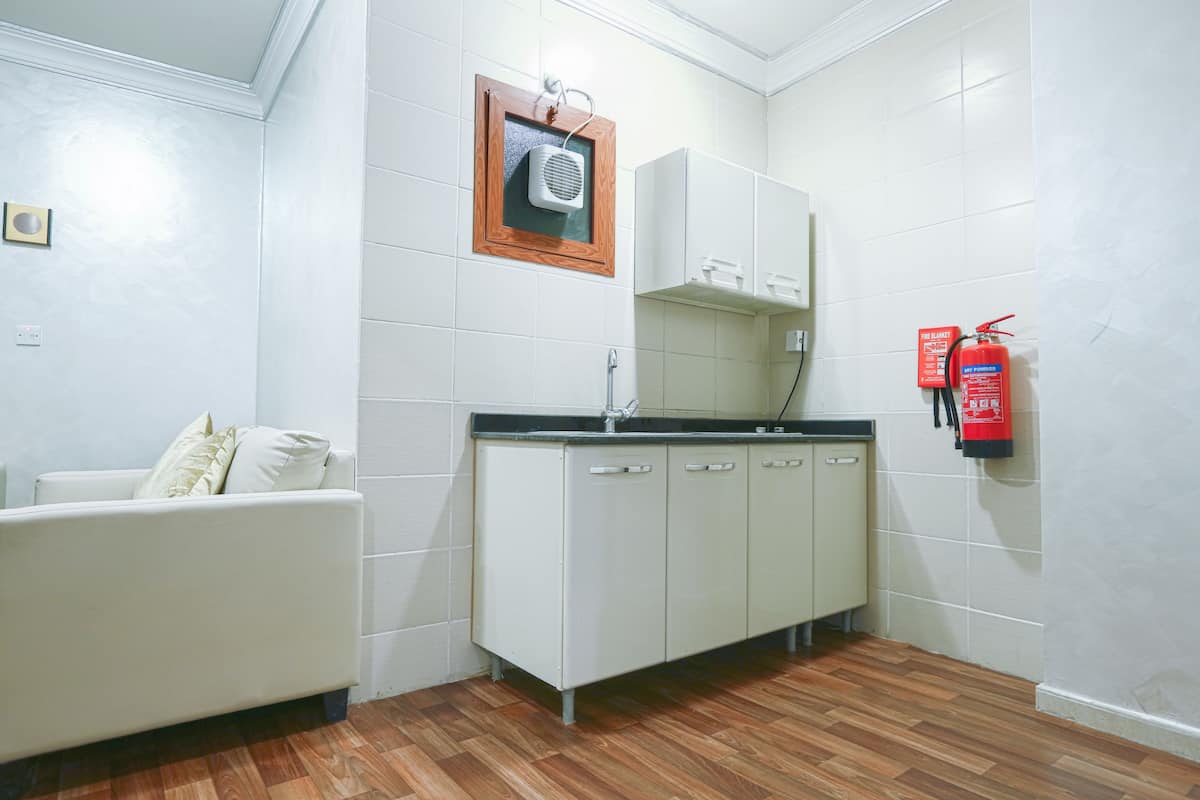A small, clean room with a kitchenette, a white sofa, and a fire extinguisher on the wall.