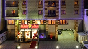 Un hotel de varios pisos con balcones, un restaurante en la planta baja y un área de estacionamiento.