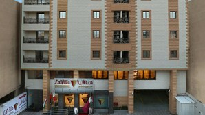 Un hotel de varios pisos con diseño moderno, que cuenta con balcones en cada planta, una alfombra roja en la entrada y un letrero que indica que es un hotel.