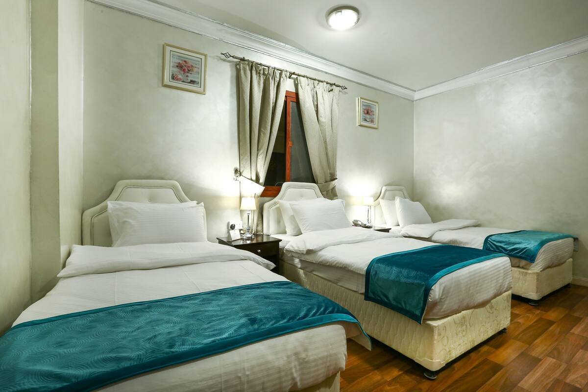 A hotel room with two beds, a nightstand, a lamp, and a window with curtains.