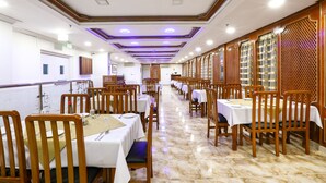 Un restaurante con mesas largas y sillas de madera, suelo de mármol e iluminación empotrada en el techo.