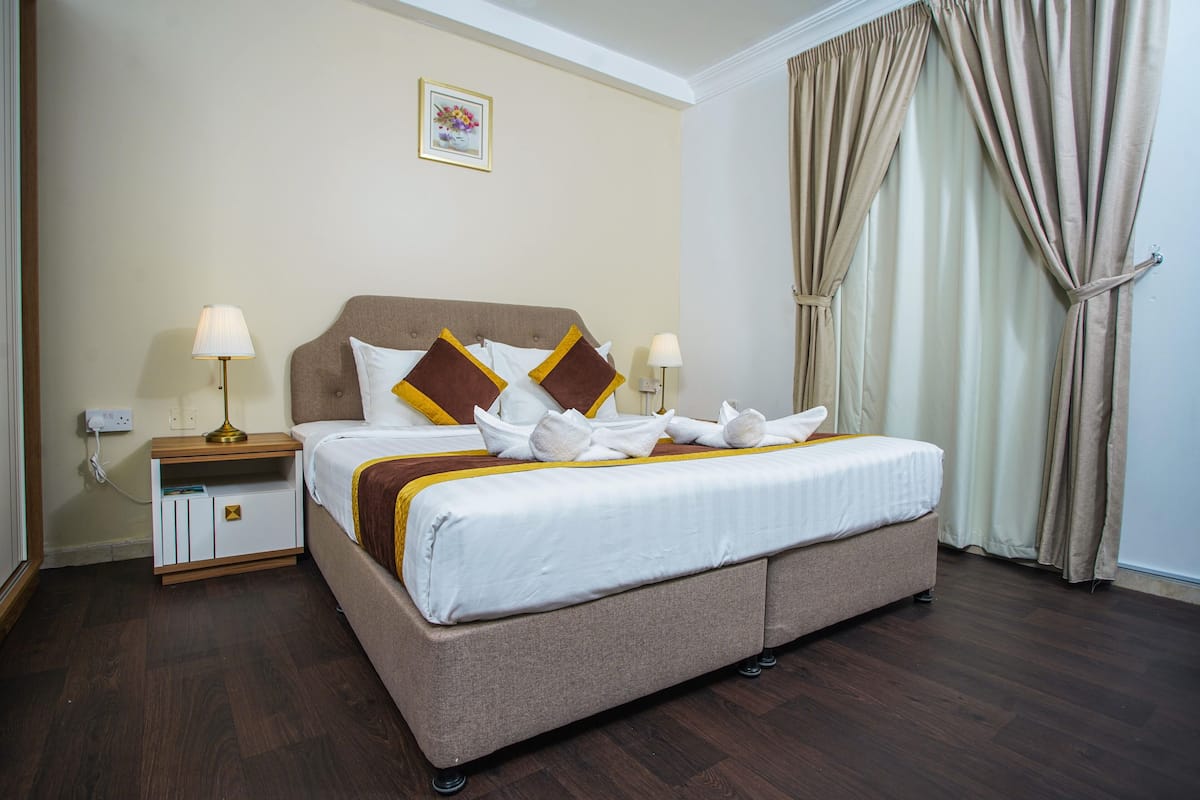 A neatly made bed with white and brown bedding, a bedside table with lamps, and a wall-mounted picture.