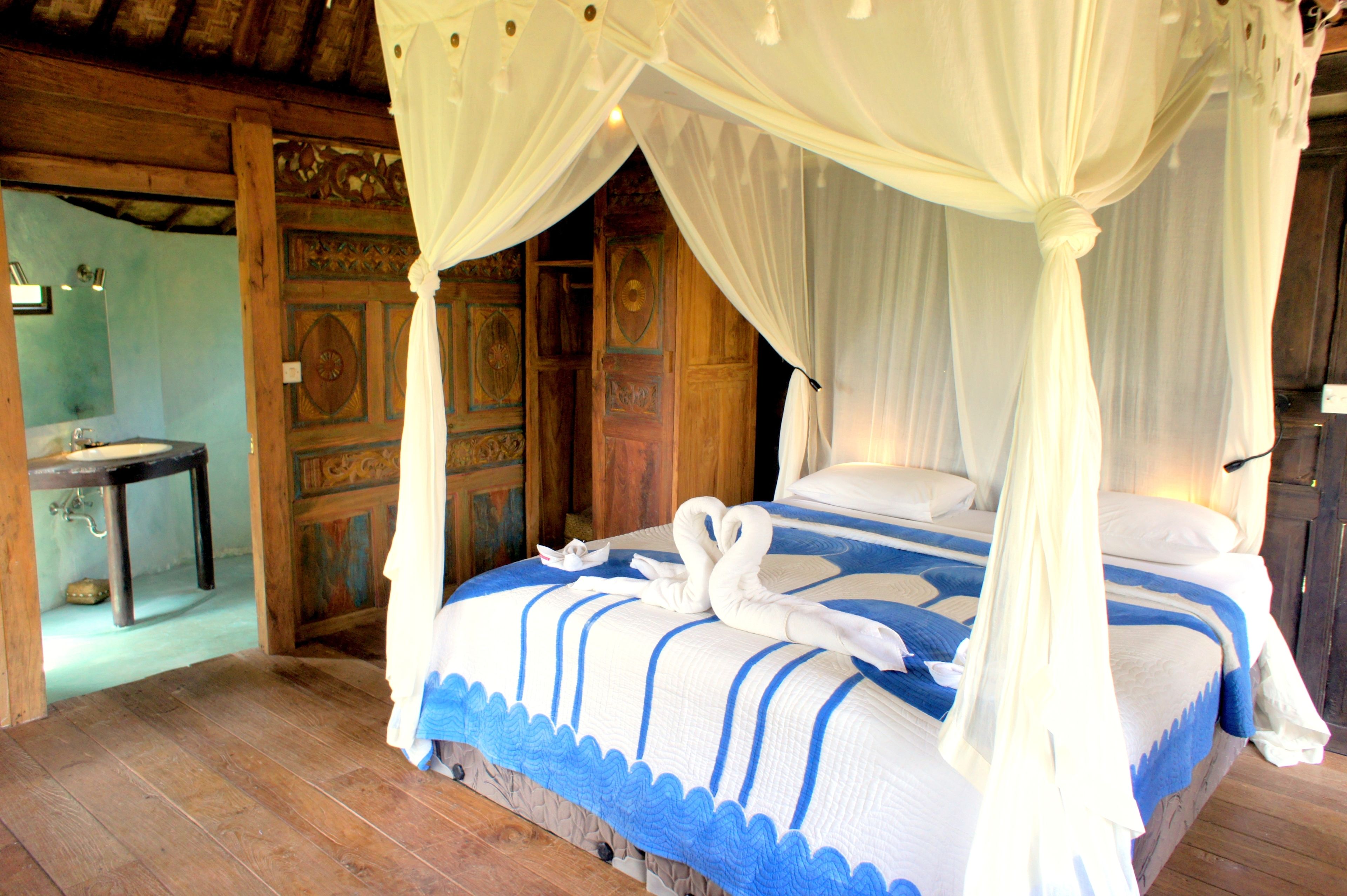 A bedroom with a canopy bed, wooden walls, and a small table with a lamp.