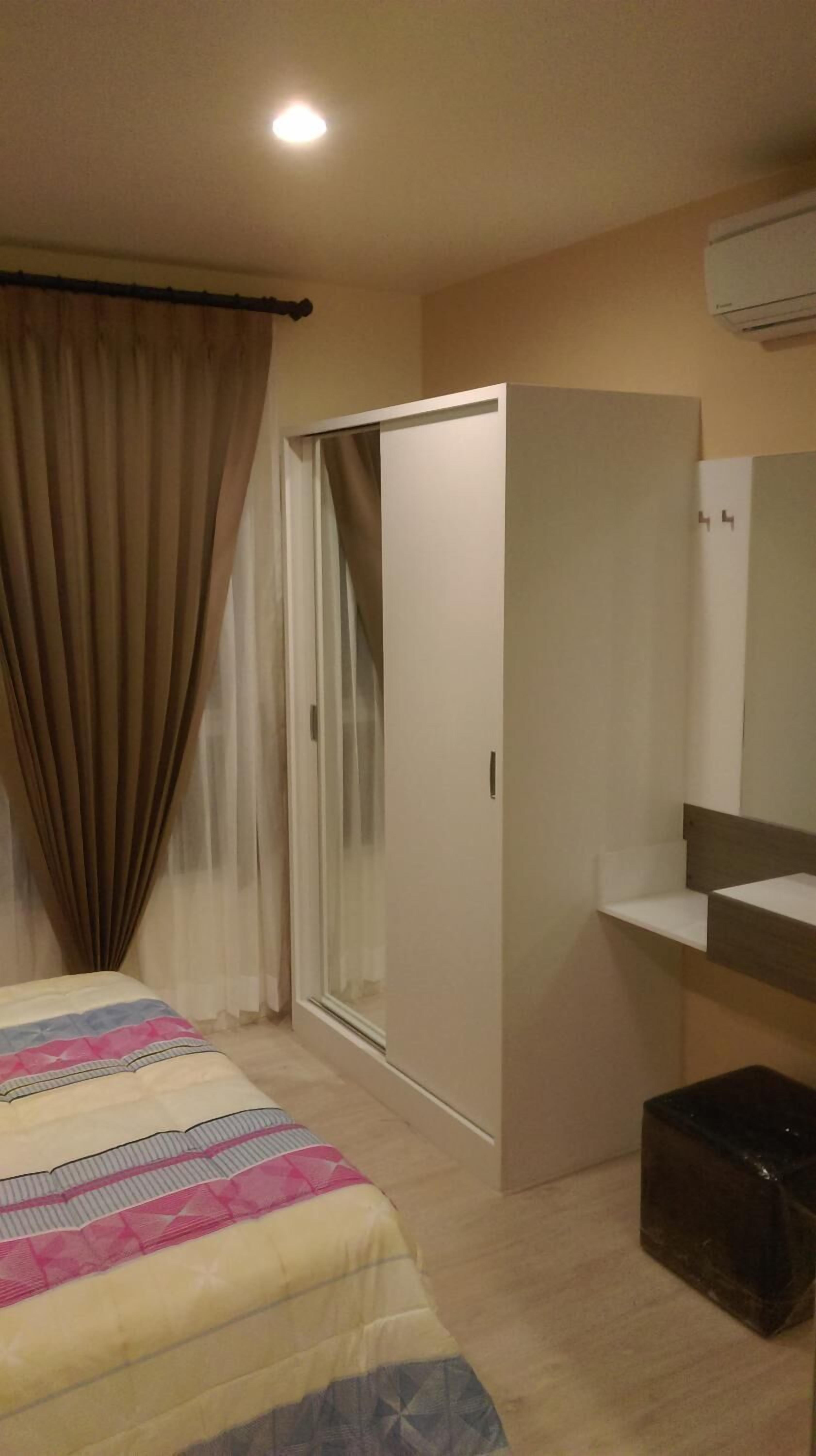 A bedroom with a bed, a wardrobe, a mirror, and a small trash bin.