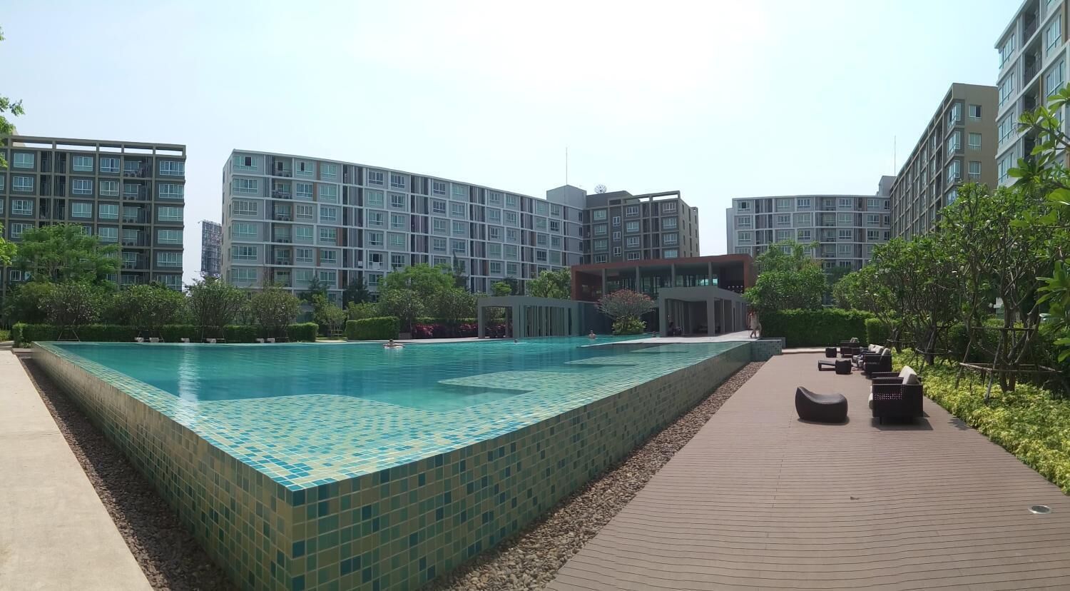 A swimming pool with tiled flooring, surrounded by a walkway and greenery.