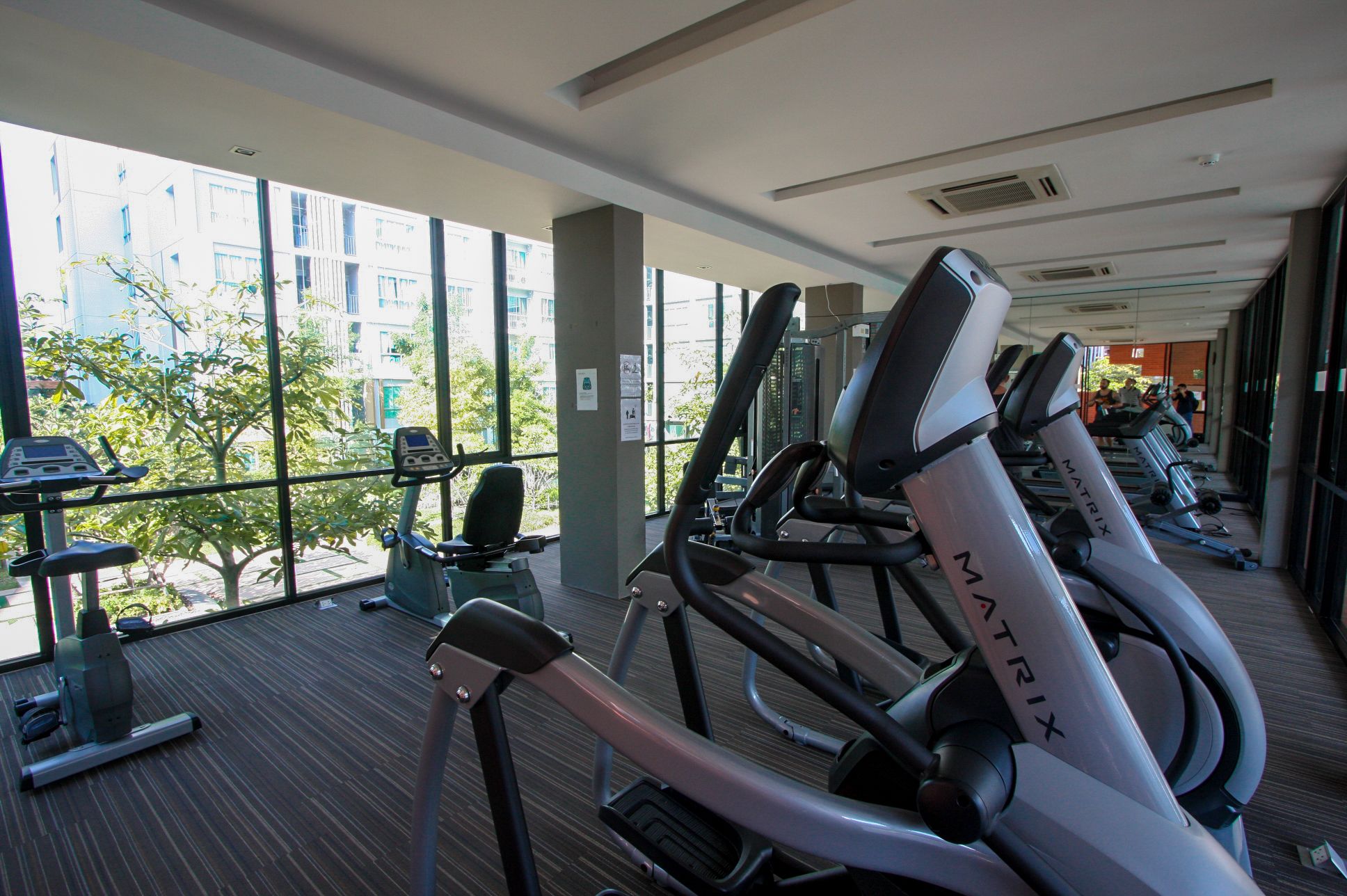 A gym with stationary bikes labeled MATRIX, large windows, and a view of buildings and trees outside.