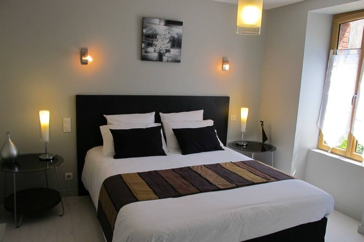 A neatly made bed with a striped blanket, two bedside tables with lamps, a wall-mounted artwork, and a window with blinds.
