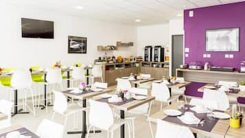 A modern dining area with white chairs and tables, a coffee station, and a purple accent wall.