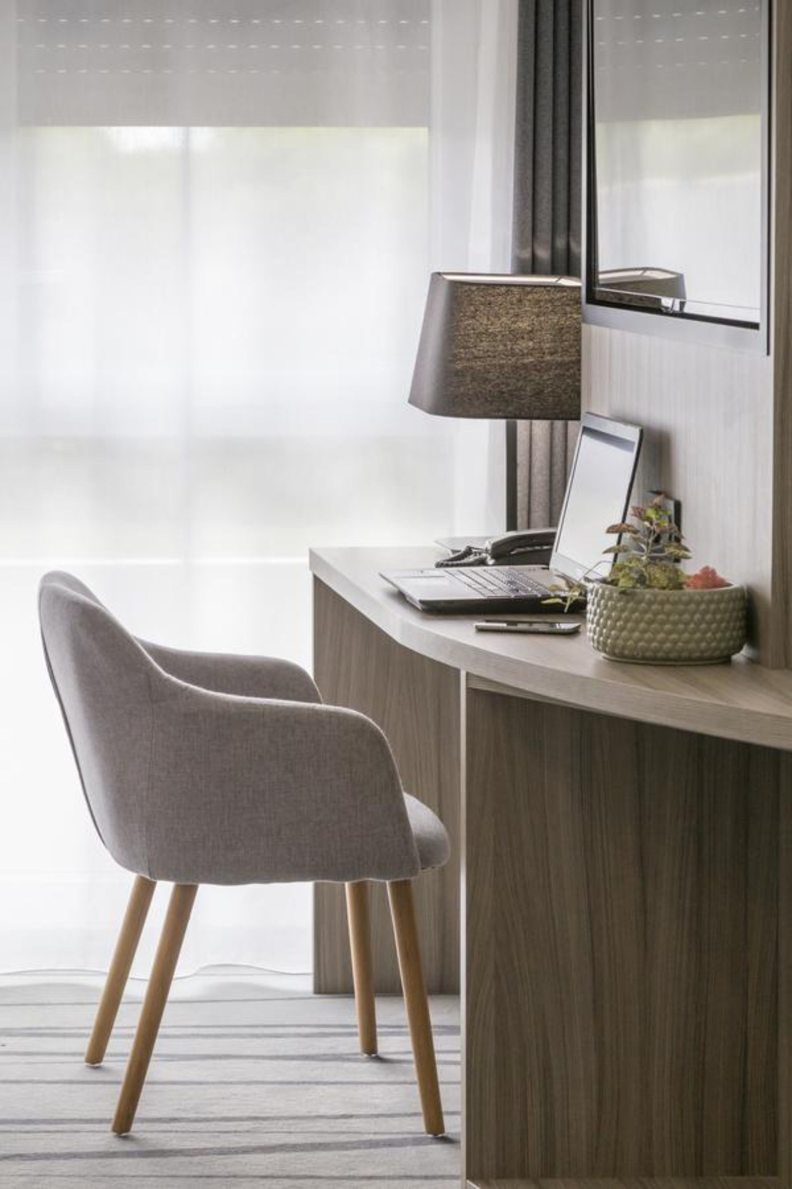 A modern workspace with a laptop, a lamp, and a potted plant on a wooden desk.