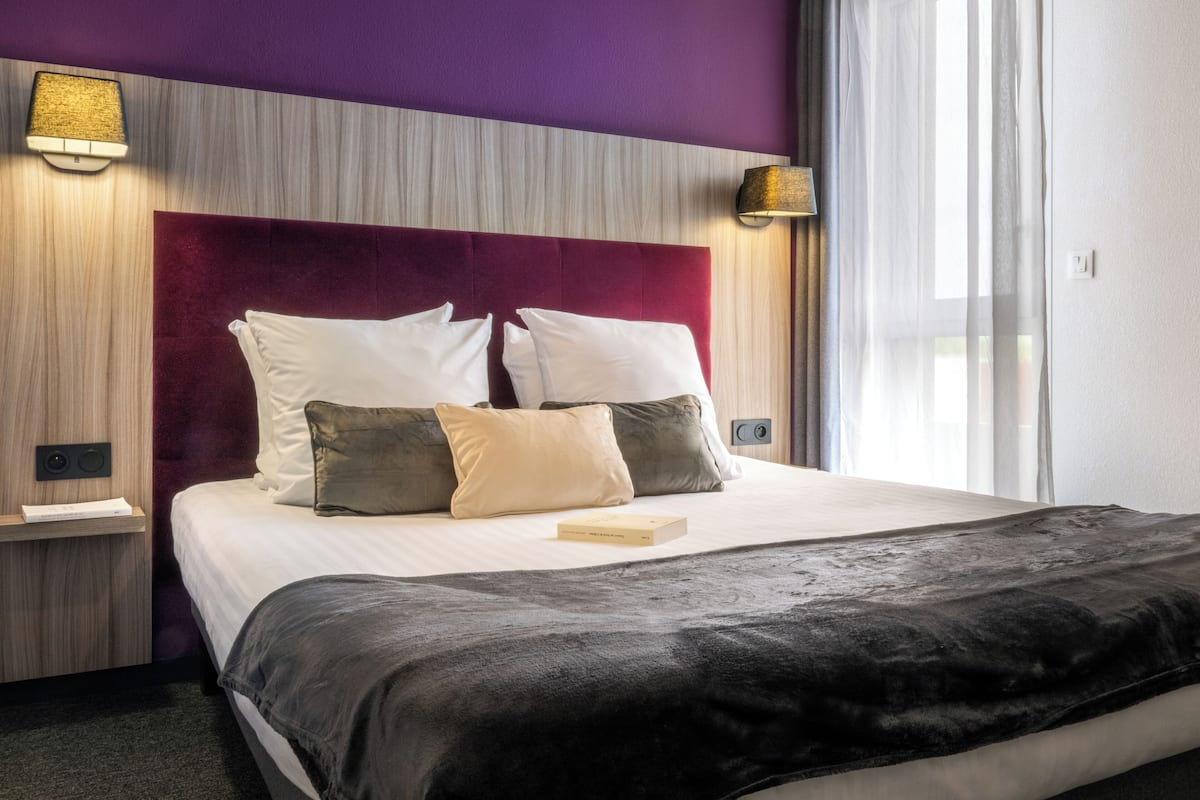 Een hotelkamer met een groot bed, een hoofdbord met een licht houten afwerking en twee wandlampen.
