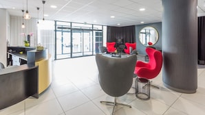 Un espace d’accueil moderne avec un comptoir d’accueil incurvé, un grand miroir et des chaises rouges.
