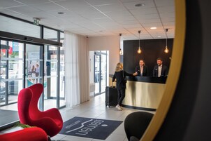 Zona de recepción de hotel con un diseño moderno, que incluye un mostrador de recepción, una silla roja y una silla negra.