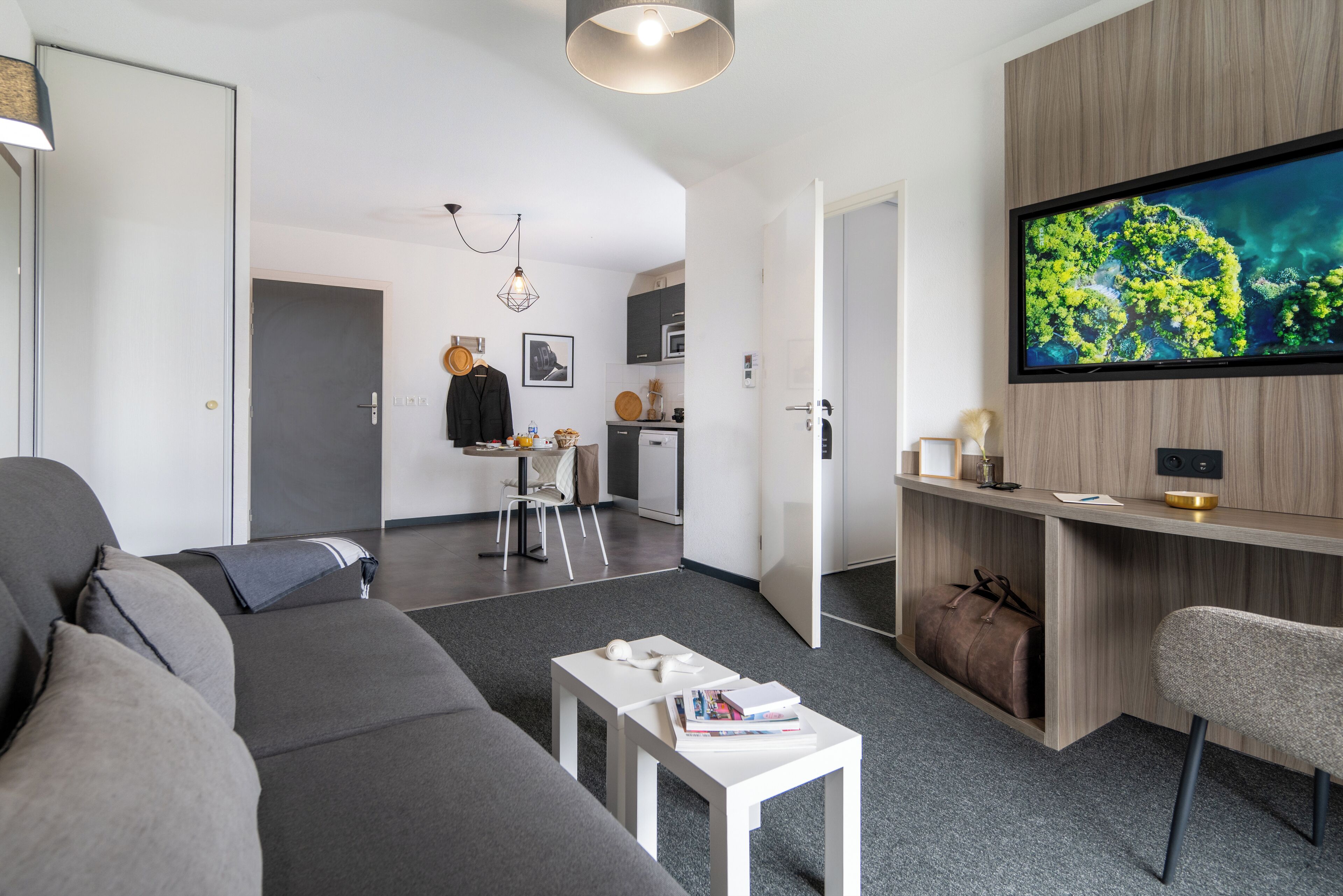 Una sala de estar moderna con un sofá gris, una mesa de centro blanca y un televisor montado en una pared de madera.
