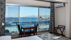 A hotel room with a large sliding glass door leading to a balcony with a view of the sea and distant mountains. - Perla Otel (Dikili)