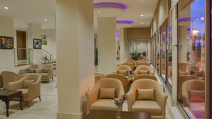 A hotel lobby with rows of beige armchairs, a coffee table with a vase, and a staircase in the background. - Perla Otel (Dikili)