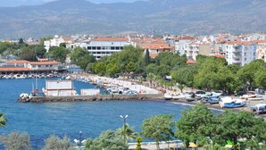 A coastal town with a marina, buildings with red roofs, and a mountainous backdrop. - Perla Otel (Dikili)