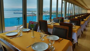 A dining area with tables set for service, large windows offering a view of a body of water and distant land. - Perla Otel (Dikili)