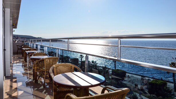 A balcony with wicker chairs and tables overlooking a body of water. - Perla Otel (Dikili)