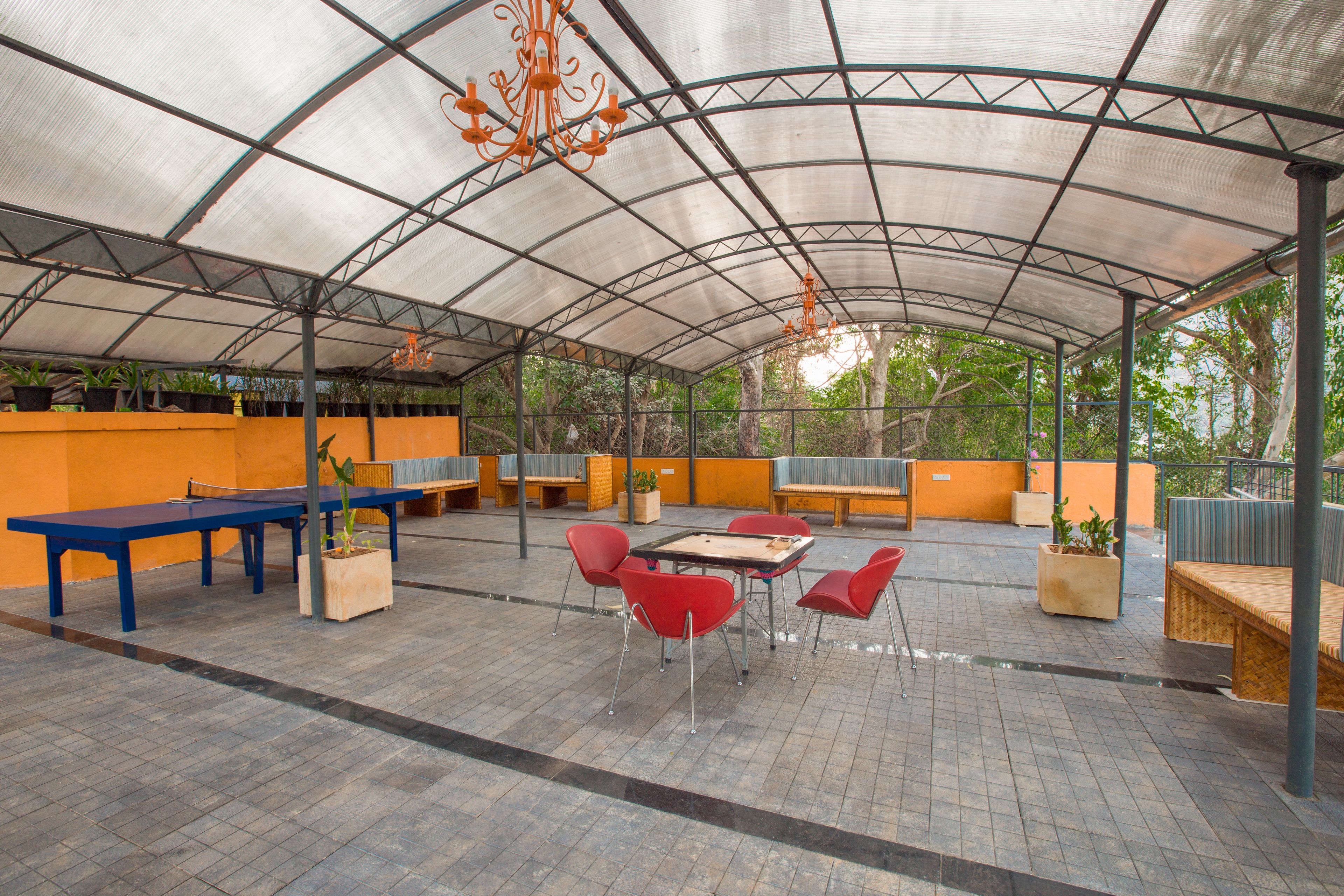 An outdoor covered patio with tables and chairs, surrounded by orange walls and potted plants.