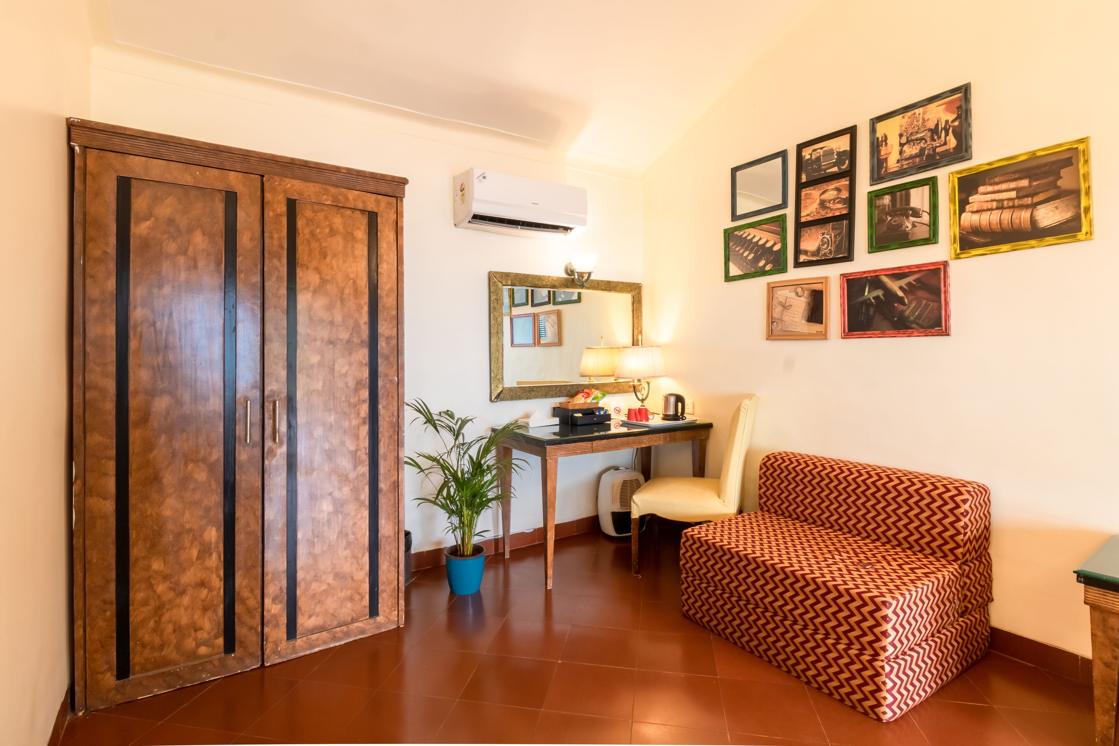 Een kamer met een garderobe, een bureau met een lamp, een stoel, een bank en verschillende afbeeldingen in lijsten aan de muur.