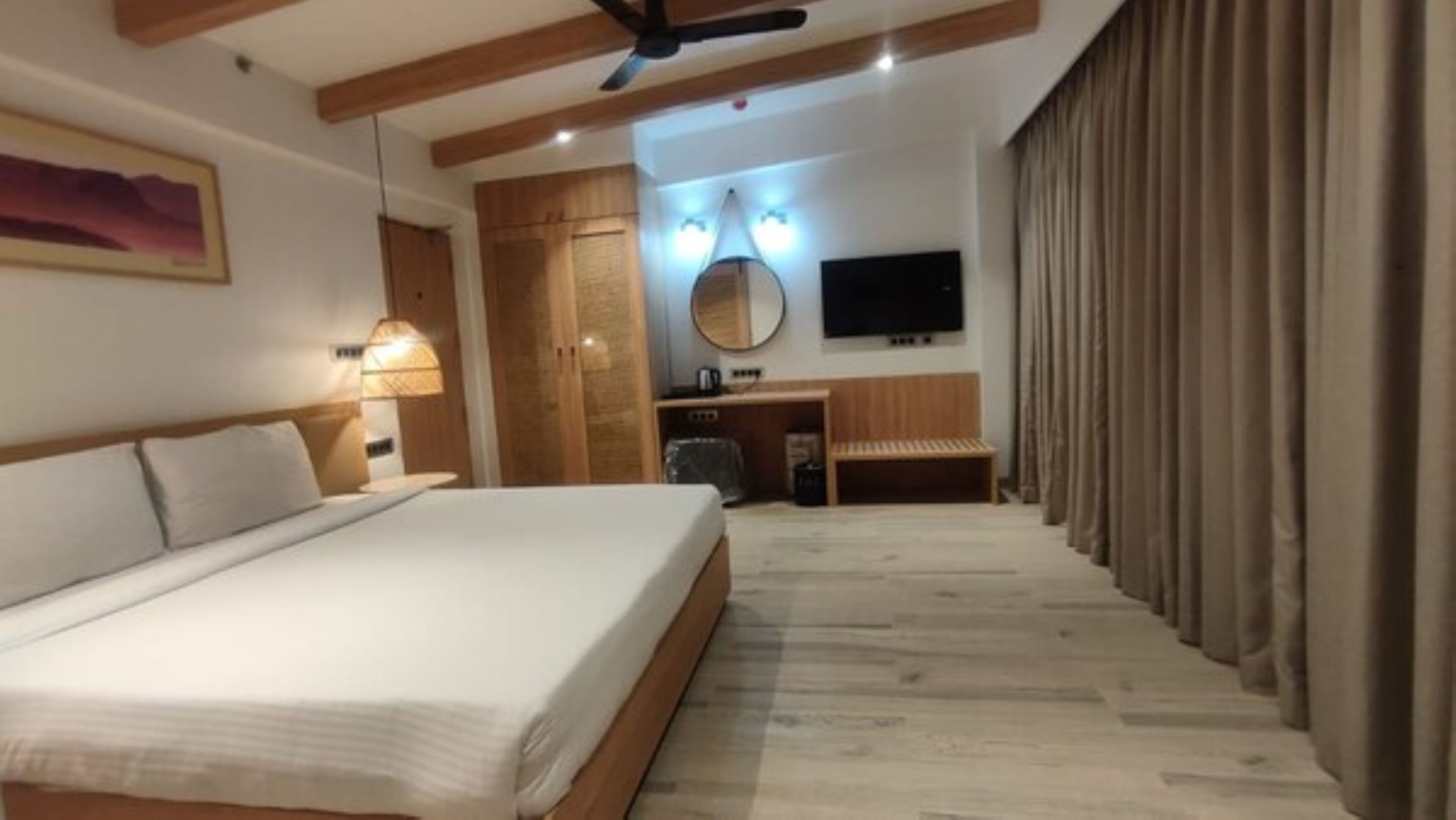 Une chambre d’hôtel avec un grand lit, un bureau avec une chaise, un téléviseur à écran plat et un ventilateur de plafond.