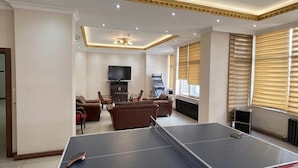 A living room with a ping pong table, sofas, a TV, and a gaming console. - Hotel Altinnal (Izmit)