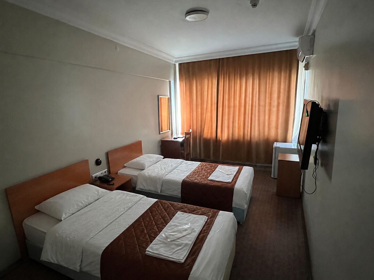 Ein Hotelzimmer mit zwei Betten, einem Schreibtisch, einem Stuhl, einem Fernseher und einem Fenster mit Vorhängen.