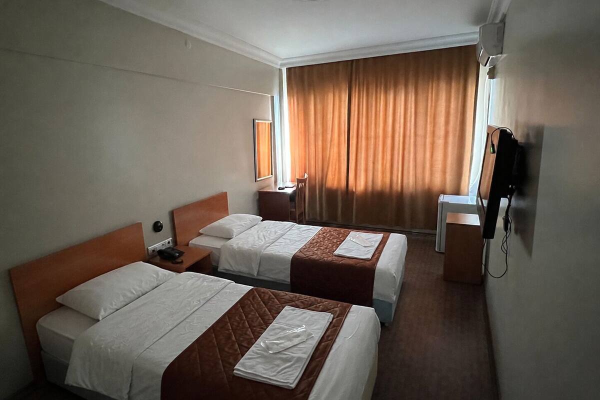 Une chambre d’hôtel avec deux lits, un bureau, une chaise, une télévision et une fenêtre avec des rideaux.
