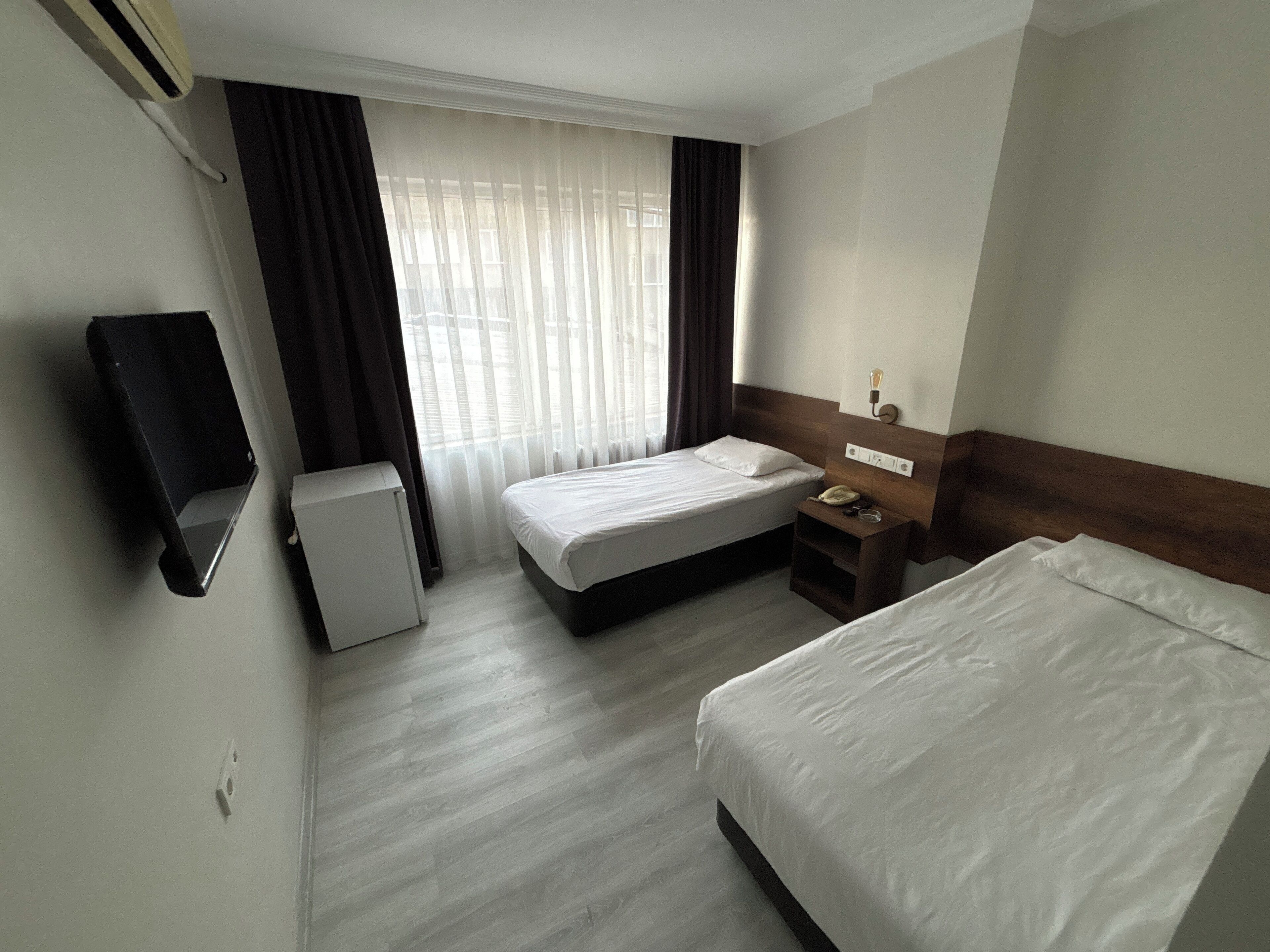 Una habitación de hotel con dos camas, un escritorio pequeño con teléfono y un televisor montado en la pared.