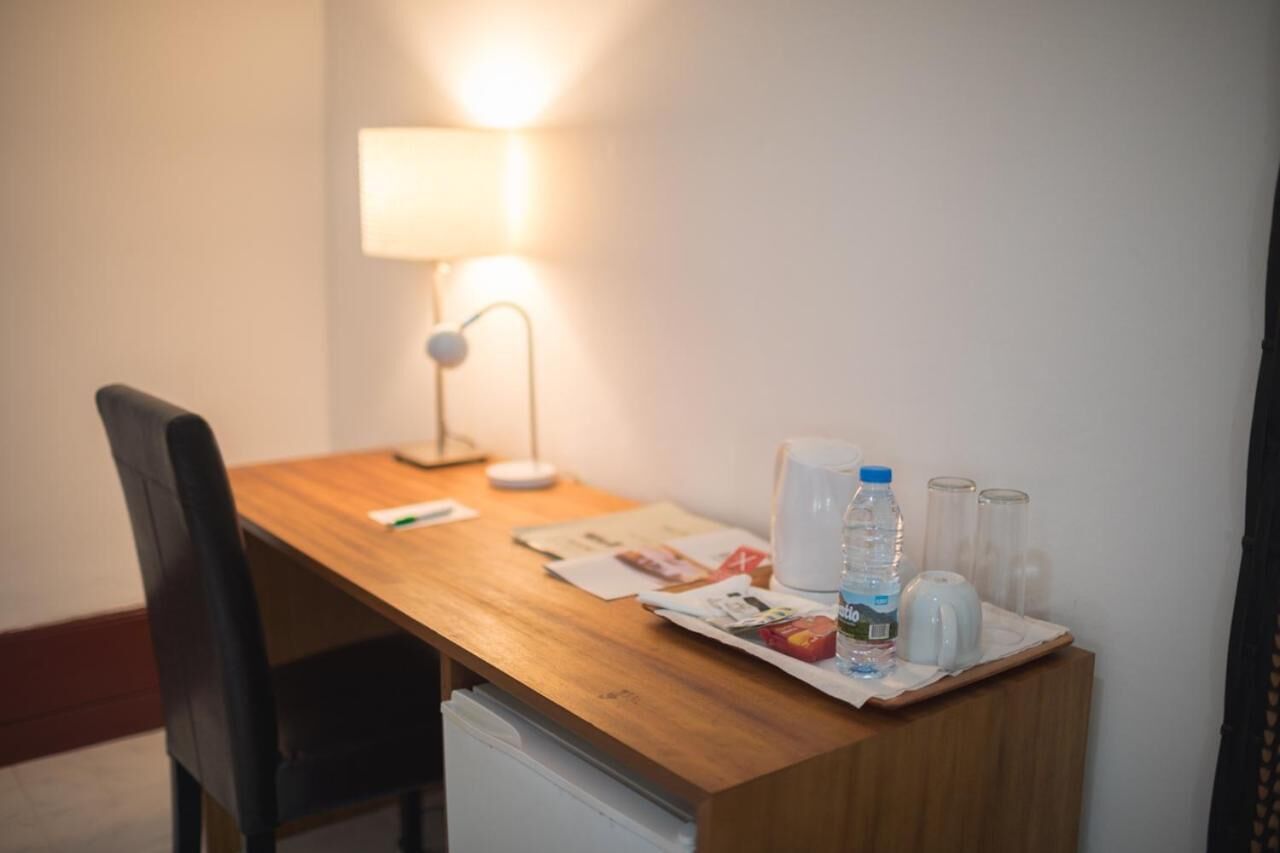 A wooden desk with a lamp, a chair, a newspaper, a water bottle, and a kettle.