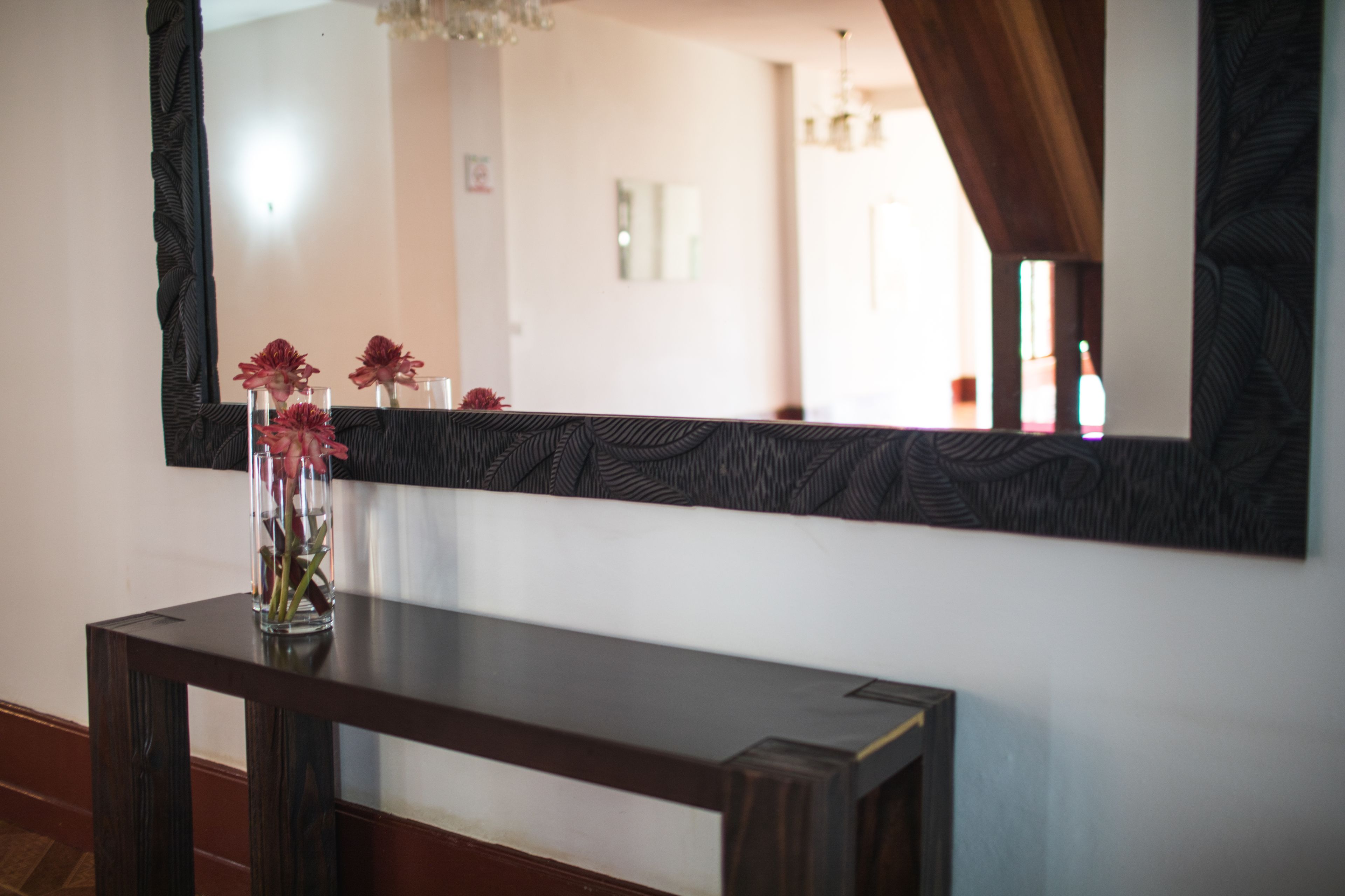 A wooden console table with a vase of flowers and a large mirror above it.