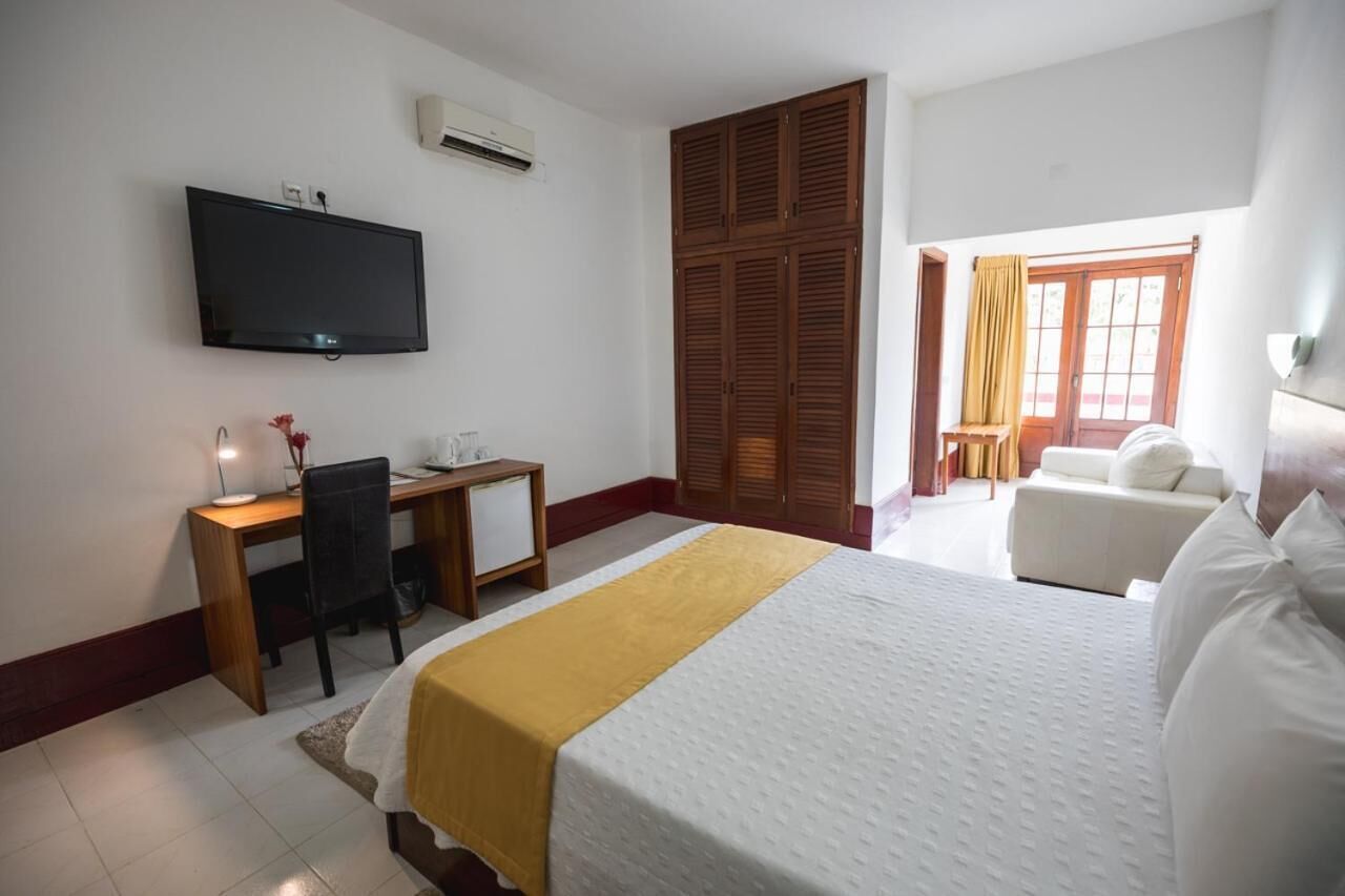 A hotel room with a bed, a desk, a chair, a television, and a wardrobe.