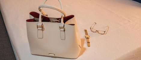 A white handbag, a pair of glasses, and a wristwatch on a bed.