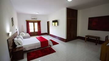 A hotel room with two beds, a red carpet, a wooden bench, and a large painting on the wall.