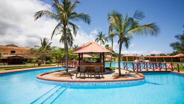 A swimming pool with a gazebo, palm trees, and a building in the background. - Hotel Praia (São Tomé)