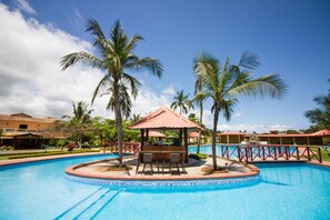 A swimming pool with a gazebo, palm trees, and a building in the background. - Hotel Praia (São Tomé)
