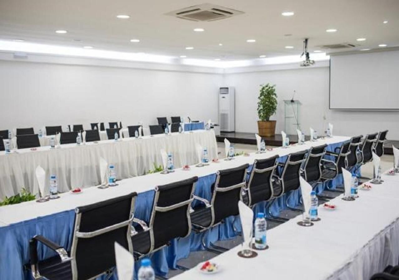 Une salle de conférence avec des rangées de tables et de chaises, un écran de projection et un appareil de climatisation.