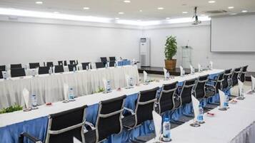 Une salle de conférence avec des rangées de tables et de chaises, un écran de projection et un appareil de climatisation.