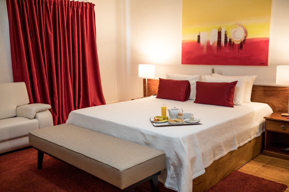 Ein Hotelzimmer mit Bett, Nachttischen, einer Bank, einem Sofa und einem Bild an der Wand.