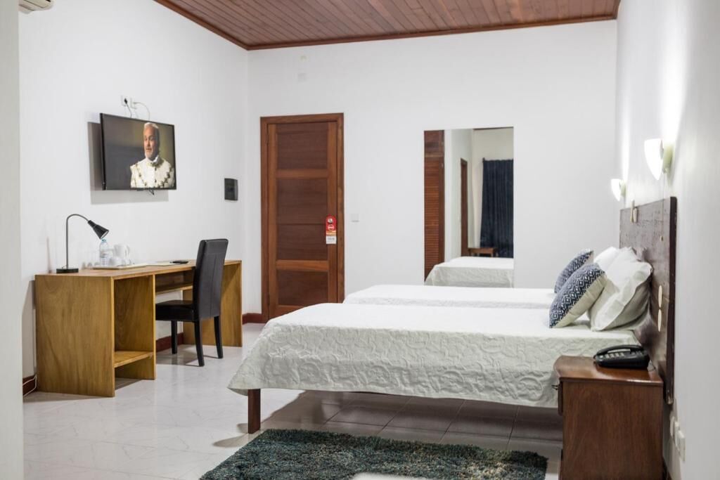 A bedroom with a wooden desk, a bed, a TV mounted on the wall, and a mirror.