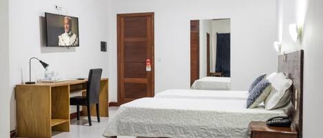 A bedroom with a wooden desk, a bed, a TV mounted on the wall, and a mirror.