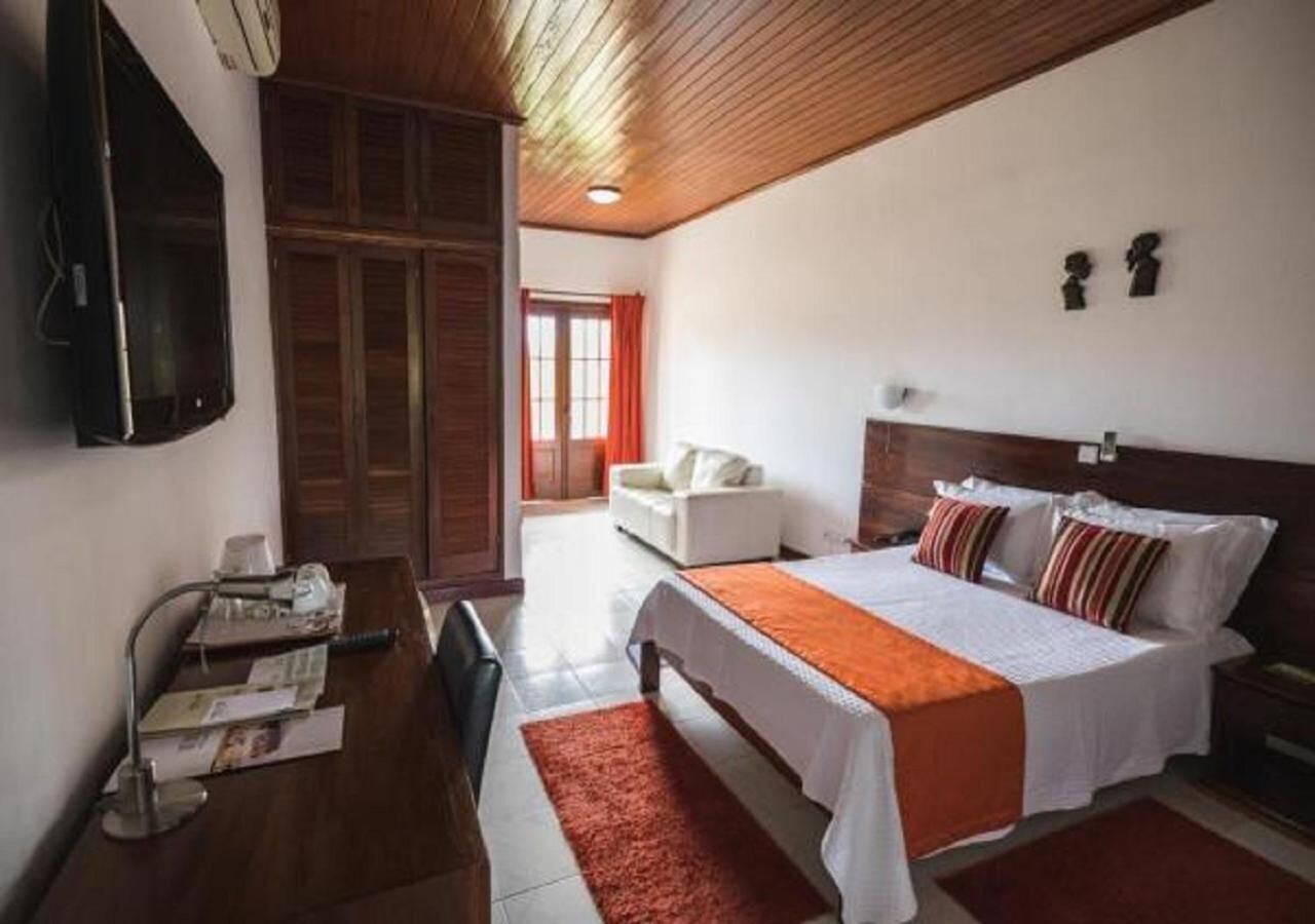 A hotel room with a bed, a desk with a lamp, a TV, and a window with curtains.