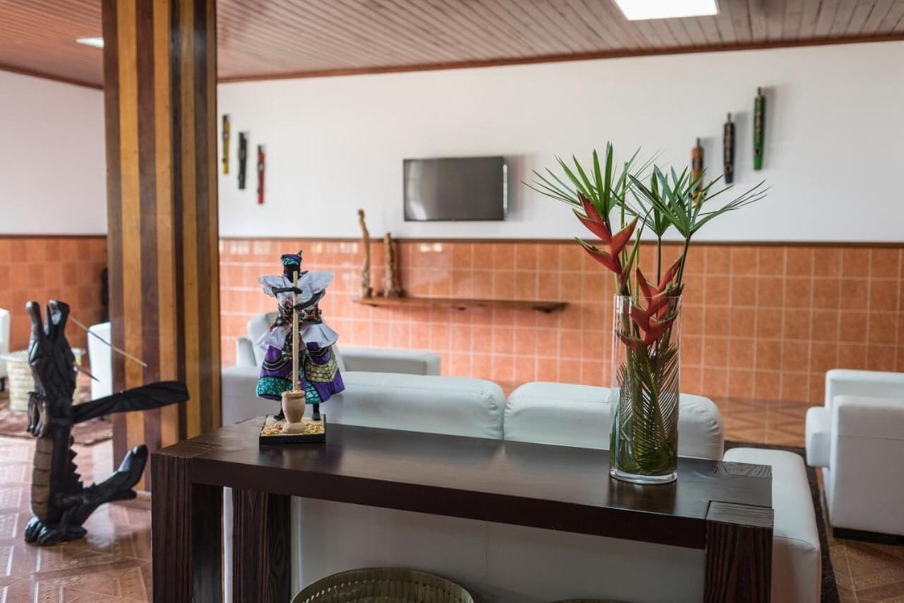 A reception area with a wooden reception desk, white sofas, a television mounted on the wall, and a decorative plant in a vase.