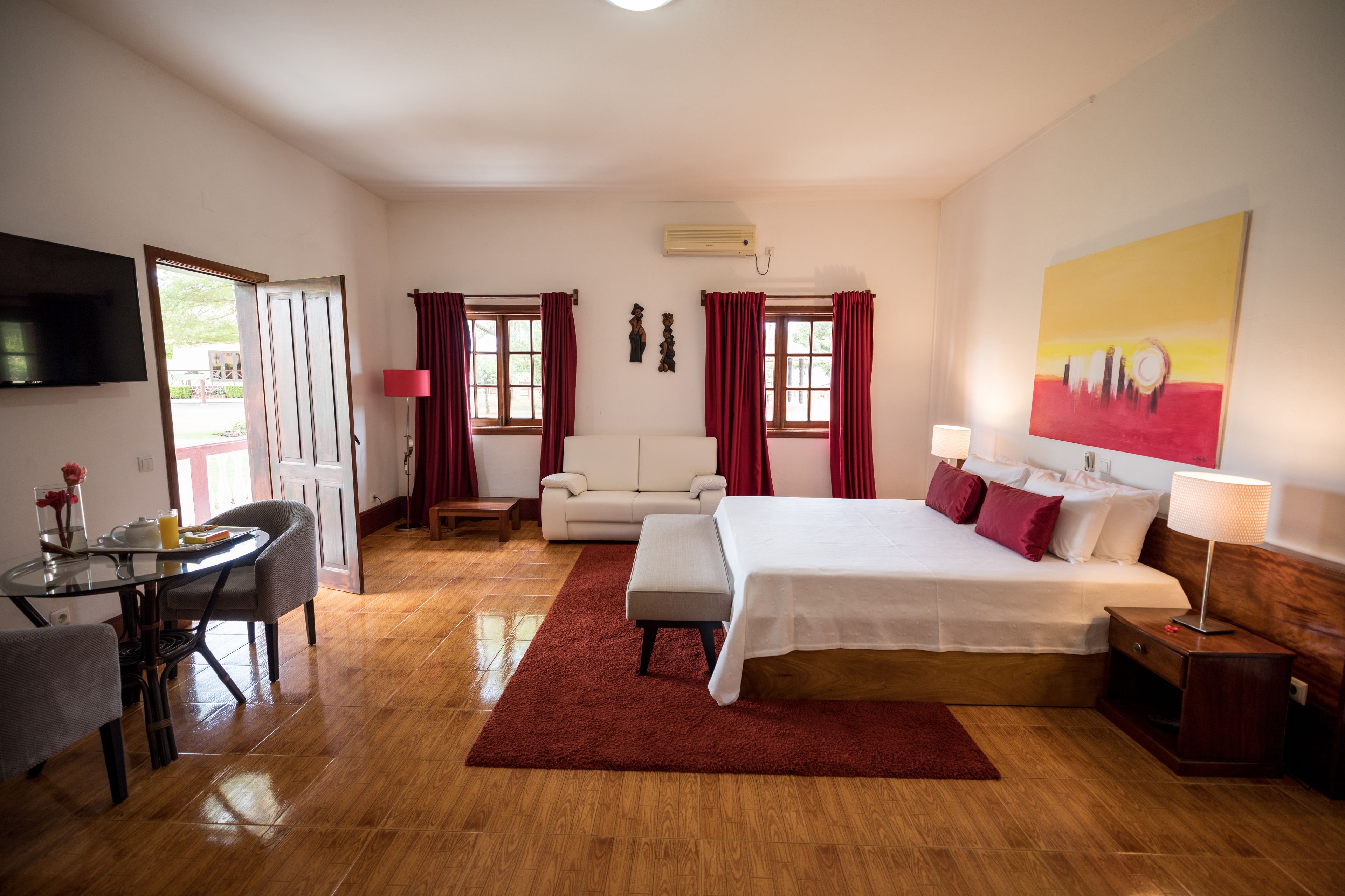 A hotel room with a bed, a sofa, a dining table, and a TV.
