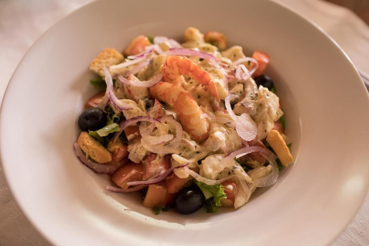 Eine Schüssel mit Meeresfrüchtesalat, Garnelen, Oliven und roten Zwiebeln.