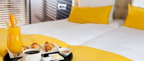 Una bandeja de desayuno bien dispuesta con croissants, café y jugo de naranja sobre una cama con ropa de cama y almohadas amarillas.